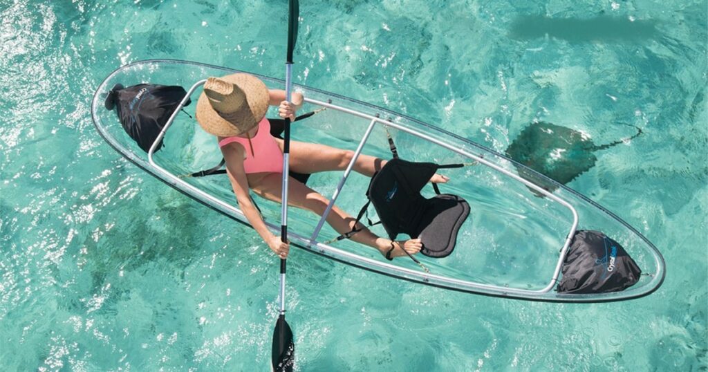 A charter guest from a superyacht using a Crystal Kayak on clear blue sea during their vacation
