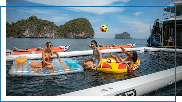 Guests relaxing and playing on a FunAir inflatable sea pool in tropical waters with dramatic limestone karst islands in the background